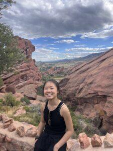 me sitting in front of beautiful jagged rust-colored rocks in the distance in Red Rocks Parks and Amphitheatre, Colorado