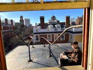A person sitting on a rooftop. The photo is framed by a window.
